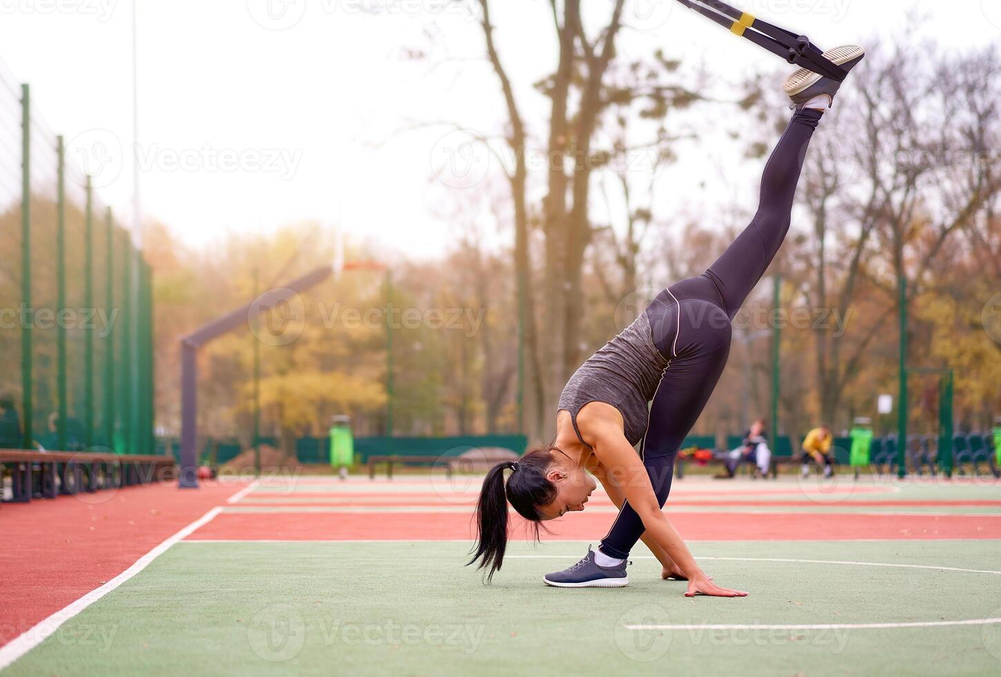 ragazza atleta funzionale formazione su Campo sportivo. misto gara giovane adulto donna fare allenarsi con sospensione sistema. salutare stile di vita. allungamento all'aperto terreno di gioco. foto