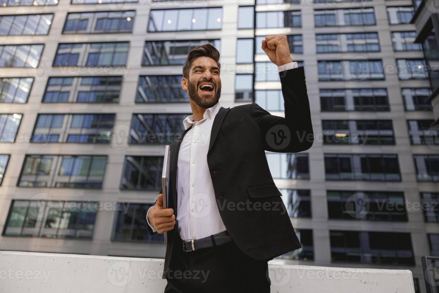 uomo d'affari con il computer portatile in piedi su ufficio terrazza e sollevato cazzotto è soddisfatto di finito progetto foto