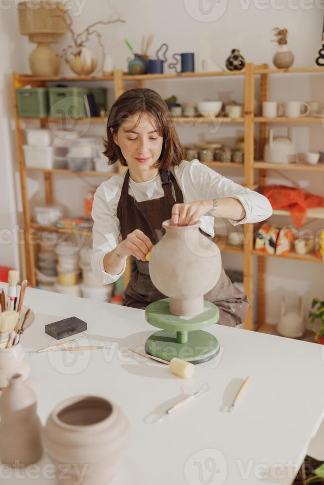 sorridente giovane femmina ceramista indossare grembiule opera con non sparato argilla vaso nel ceramica studio foto