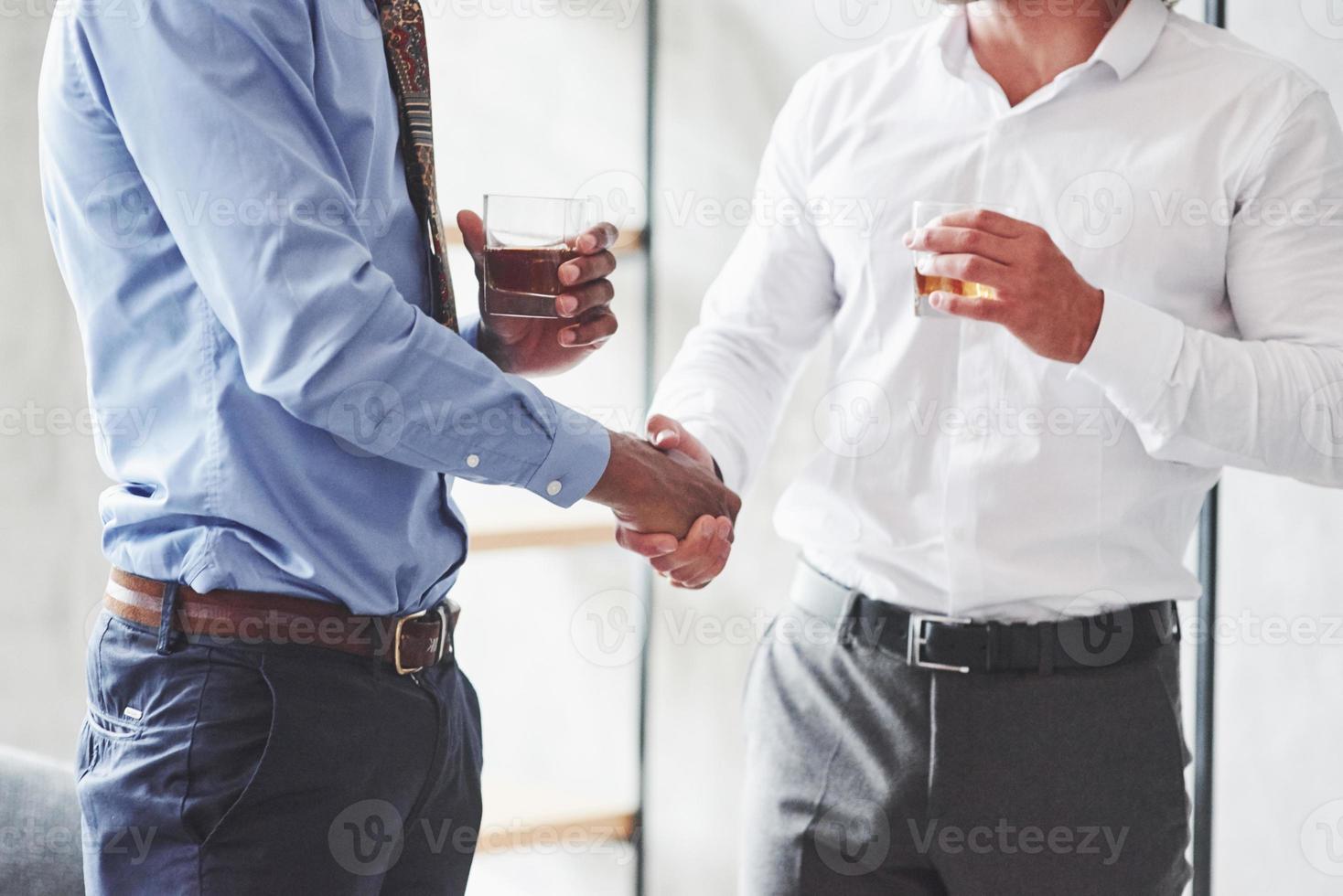 primo piano di due uomini d'affari internazionali hanno un buon affare e tengono in mano bicchieri di whisky foto