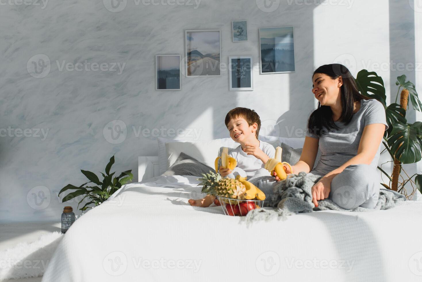 mamma con figlio nel pigiama mangiare frutta su letto. ritratto felice, sorridente, gioioso famiglia, madre e figlio avendo prima colazione nel letto, sorpresa su mamma giorno. positivo umano emozioni foto