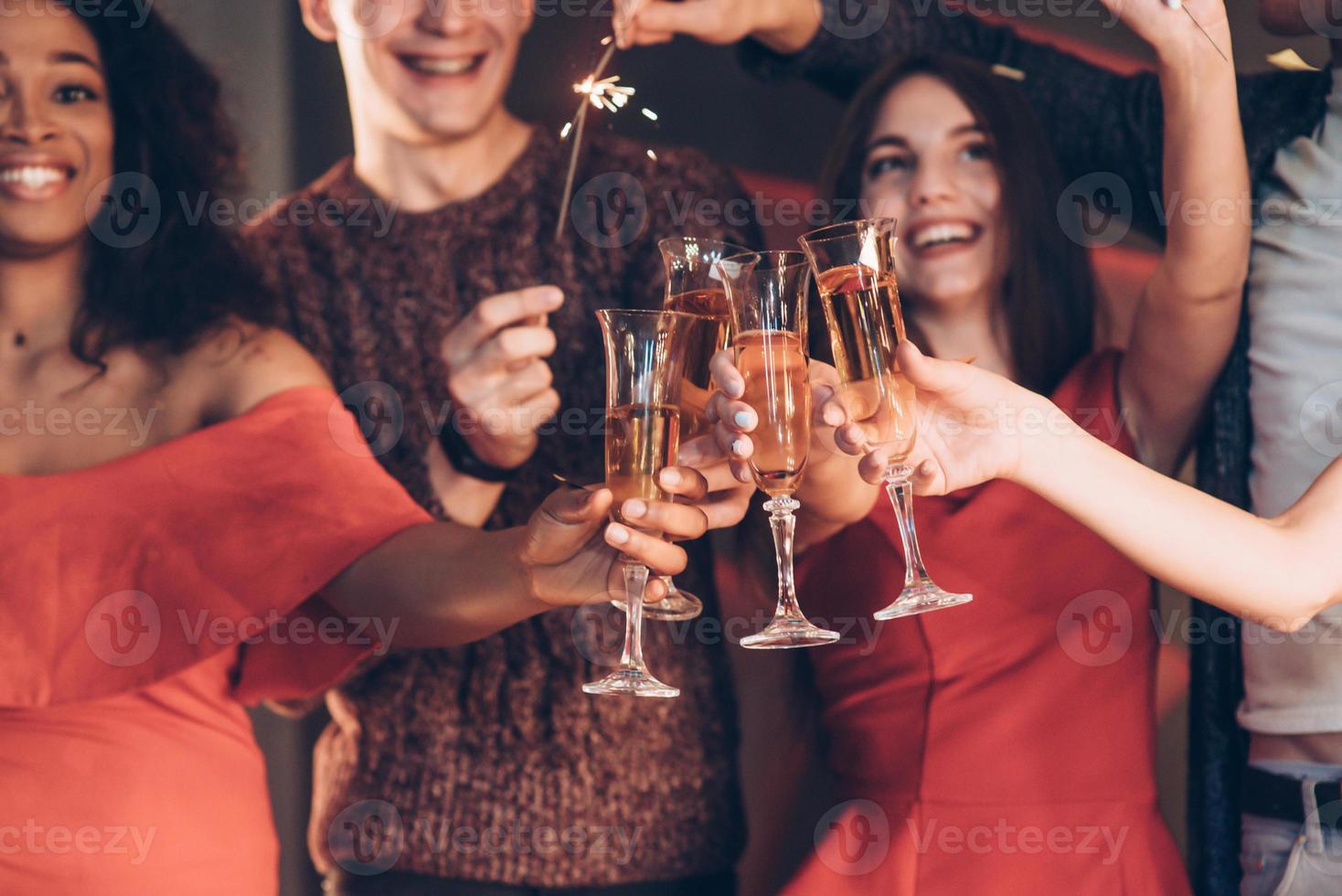 lo champagne è parte integrante. amici multirazziali festeggiano il nuovo anno e tengono in mano luci e bicchieri del Bengala con un drink foto