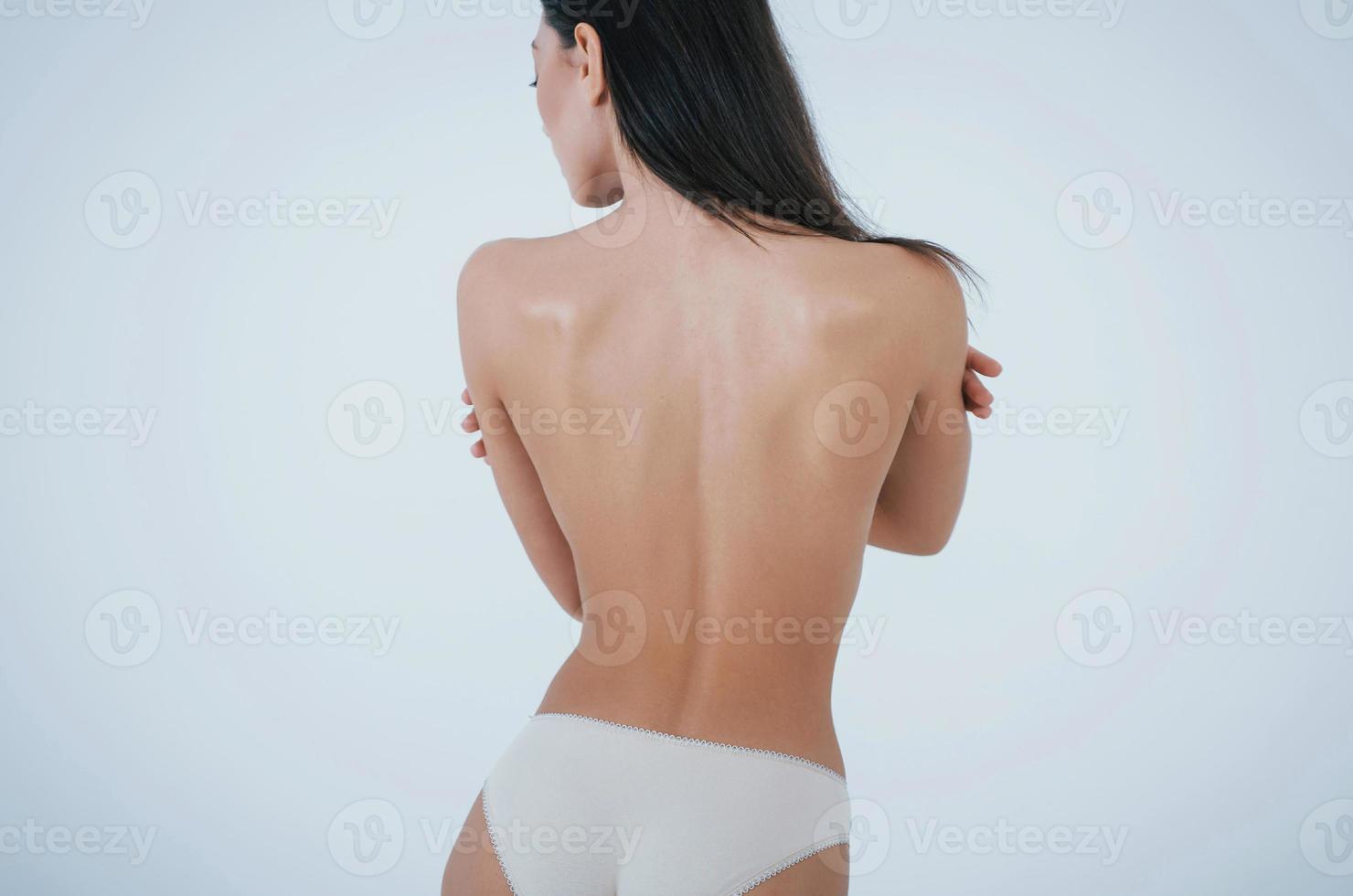 abbracciando se stessa. ragazza con un corpo perfetto in biancheria intima bianca che volta le spalle allo sfondo bianco in studio foto