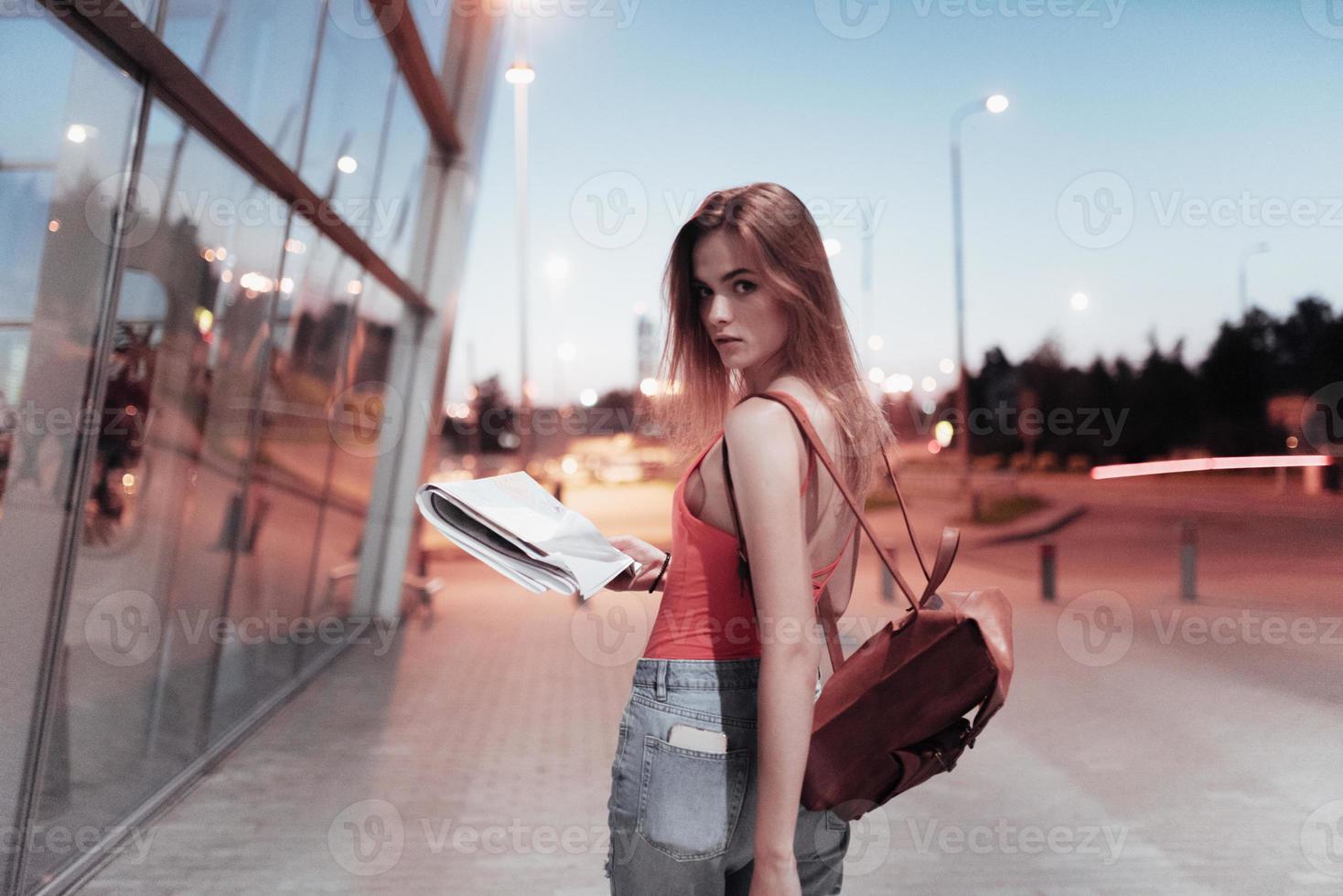 bella ragazza che cammina vicino all'edificio dell'aeroporto e tiene la mappa mentre guarda nella telecamera foto