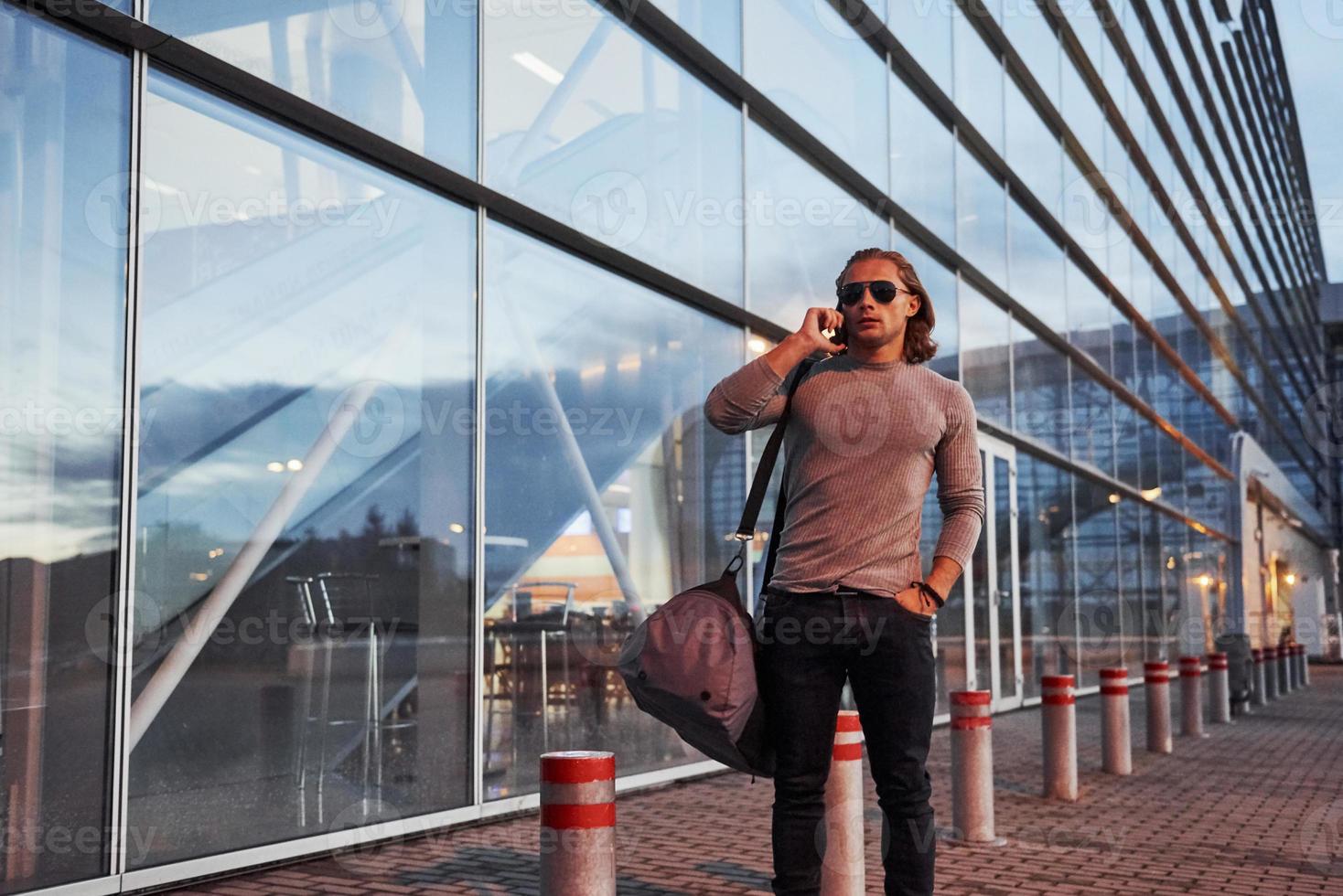 ragazzo con gli occhiali da sole che parla al telefono cellulare sull'edificio in background foto