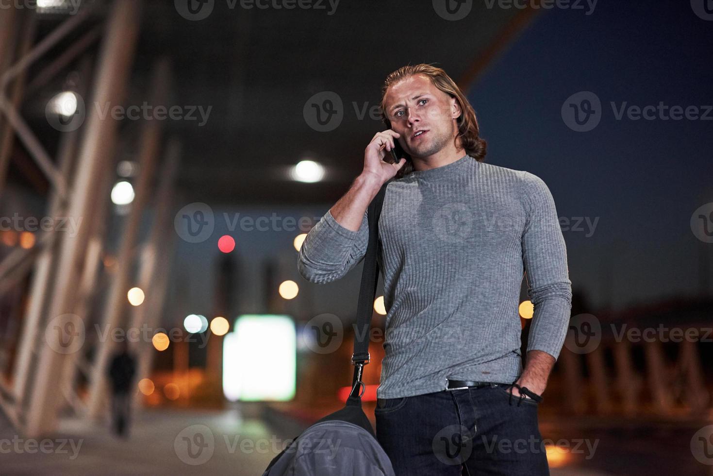 raccontando problemi al telefono. uomo con i capelli lunghi e bagaglio da viaggio in attesa che il taxi venga a prenderlo foto