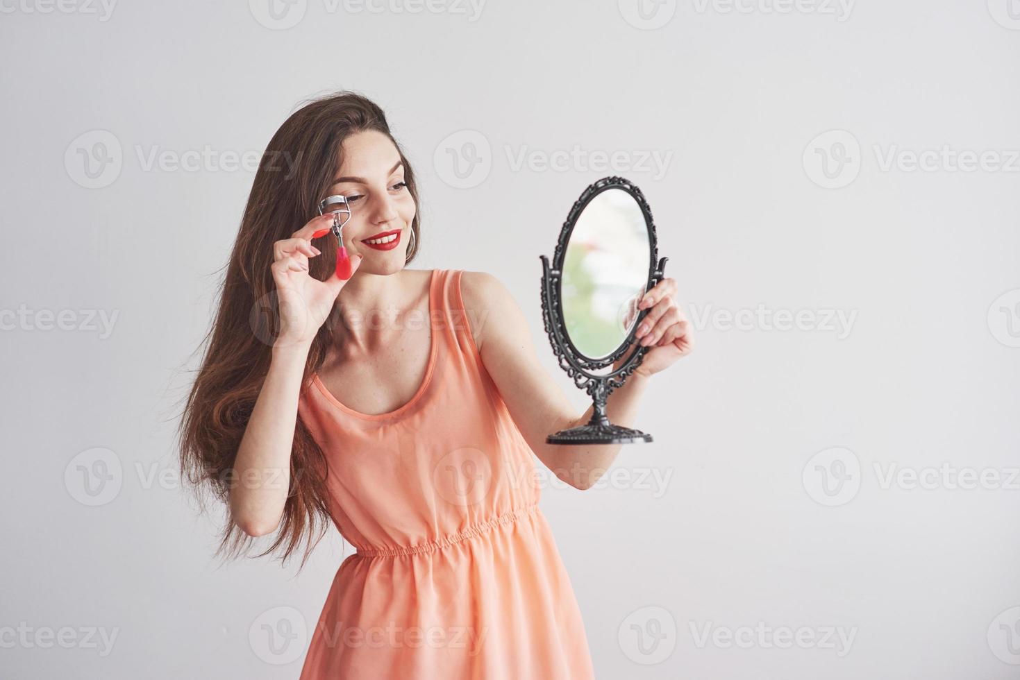 giovane bella donna che tiene uno specchio e guarda lo strumento delle sopracciglia foto