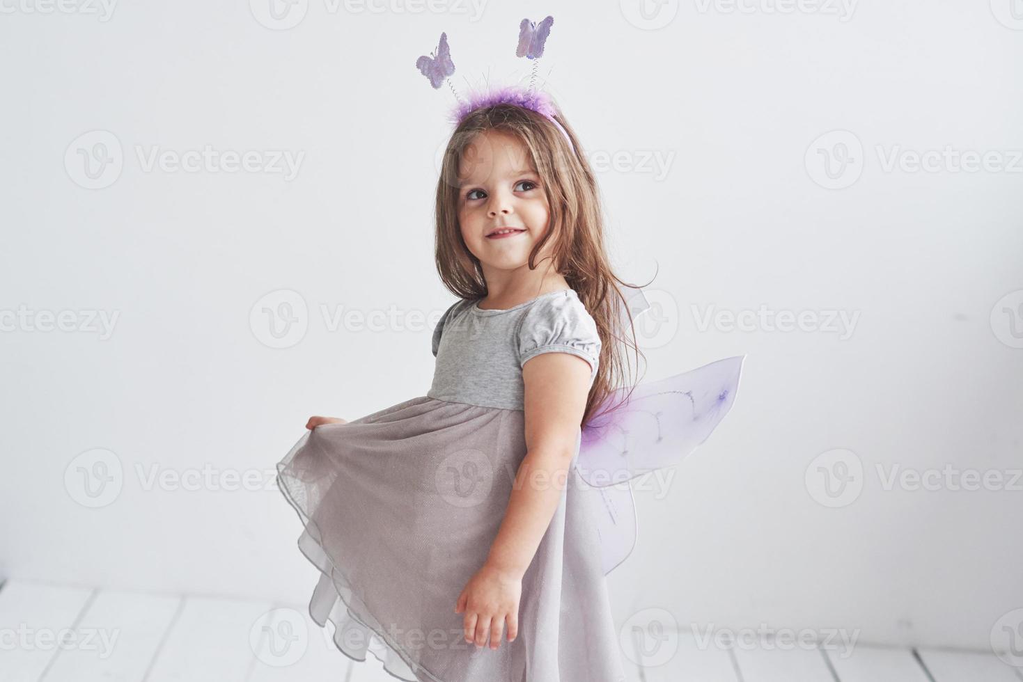 sguardo sognante. l'immaginazione è una cosa potente. adorabile bambina in costume da fata in piedi in una stanza con sfondo bianco foto