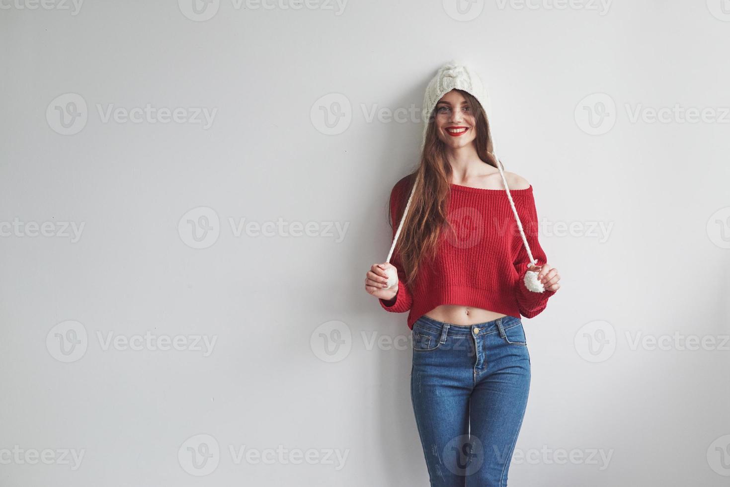 sembra che sia la sua cosa. ragazza divertente in maglione lavorato a maglia e cappello in piedi al chiuso con sfondo bianco foto