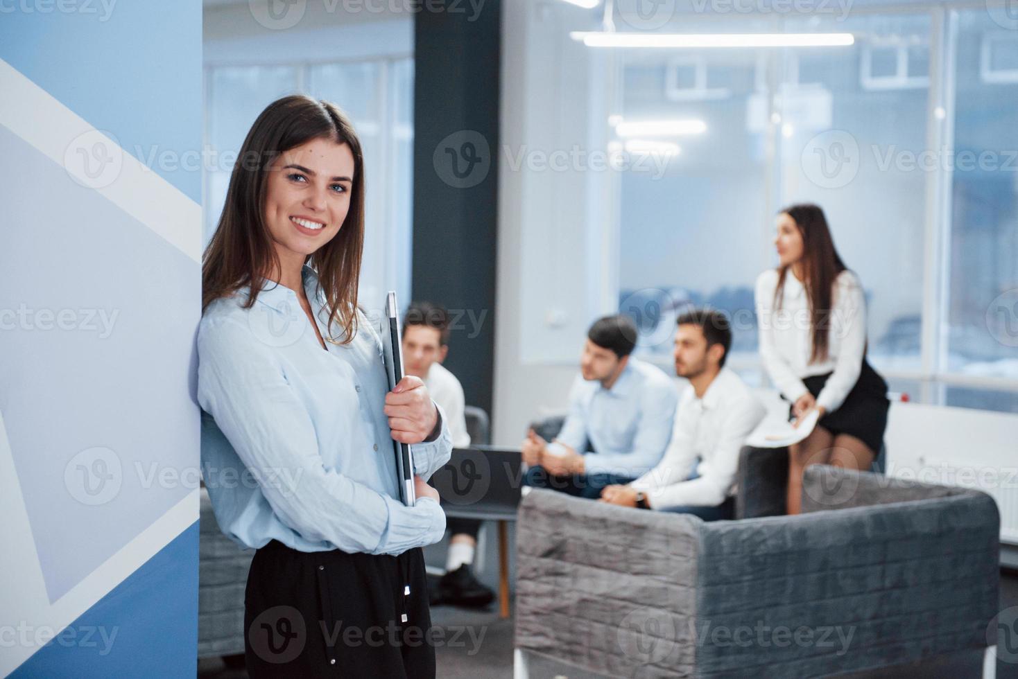 bellissimo interno moderno. ritratto di giovane ragazza in piedi in ufficio con i dipendenti in background foto