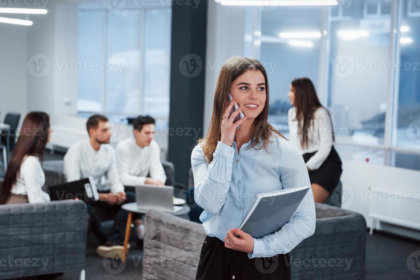 ha un accordo. ritratto di giovane ragazza in piedi in ufficio con i dipendenti in background foto