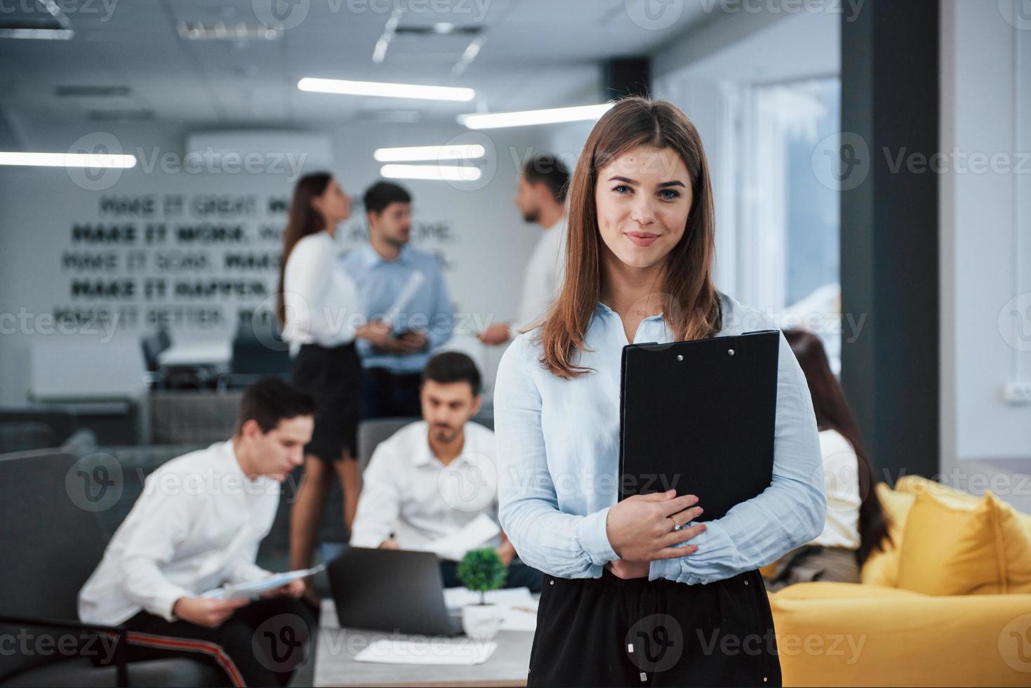 concezione del successo. ritratto di giovane ragazza in piedi in ufficio con i dipendenti in background foto