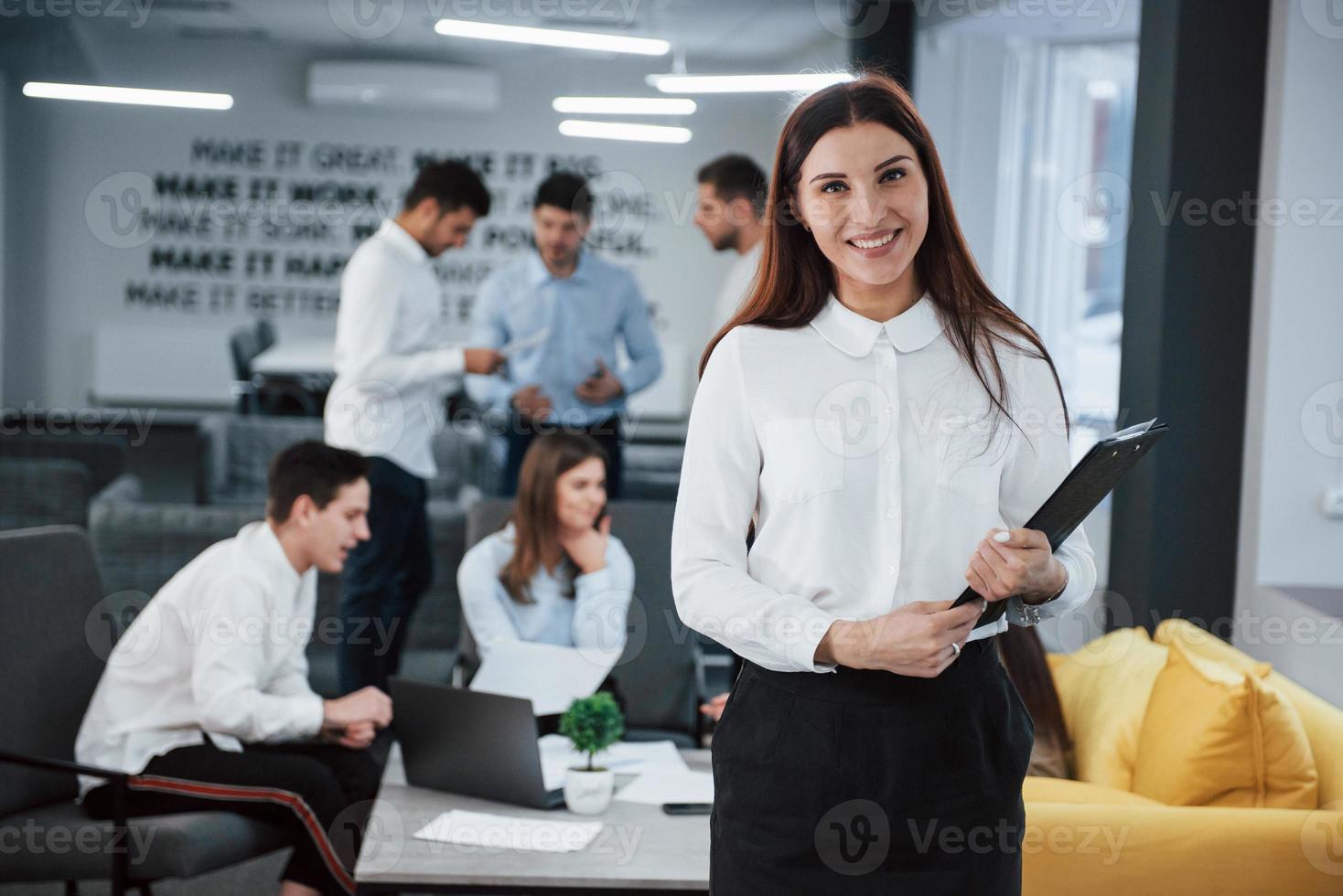 consulente aziendale è pronto per il lavoro. ritratto di giovane ragazza in piedi in ufficio con i dipendenti in background foto