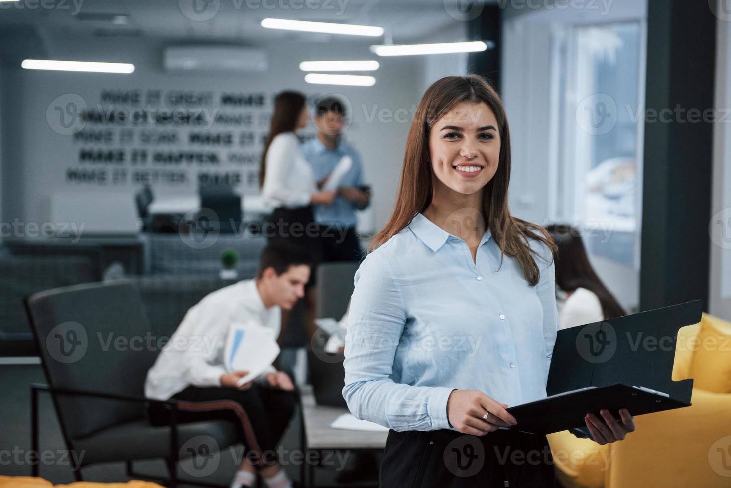 bella donna allegra. ritratto di giovane ragazza in piedi in ufficio con i dipendenti in background foto