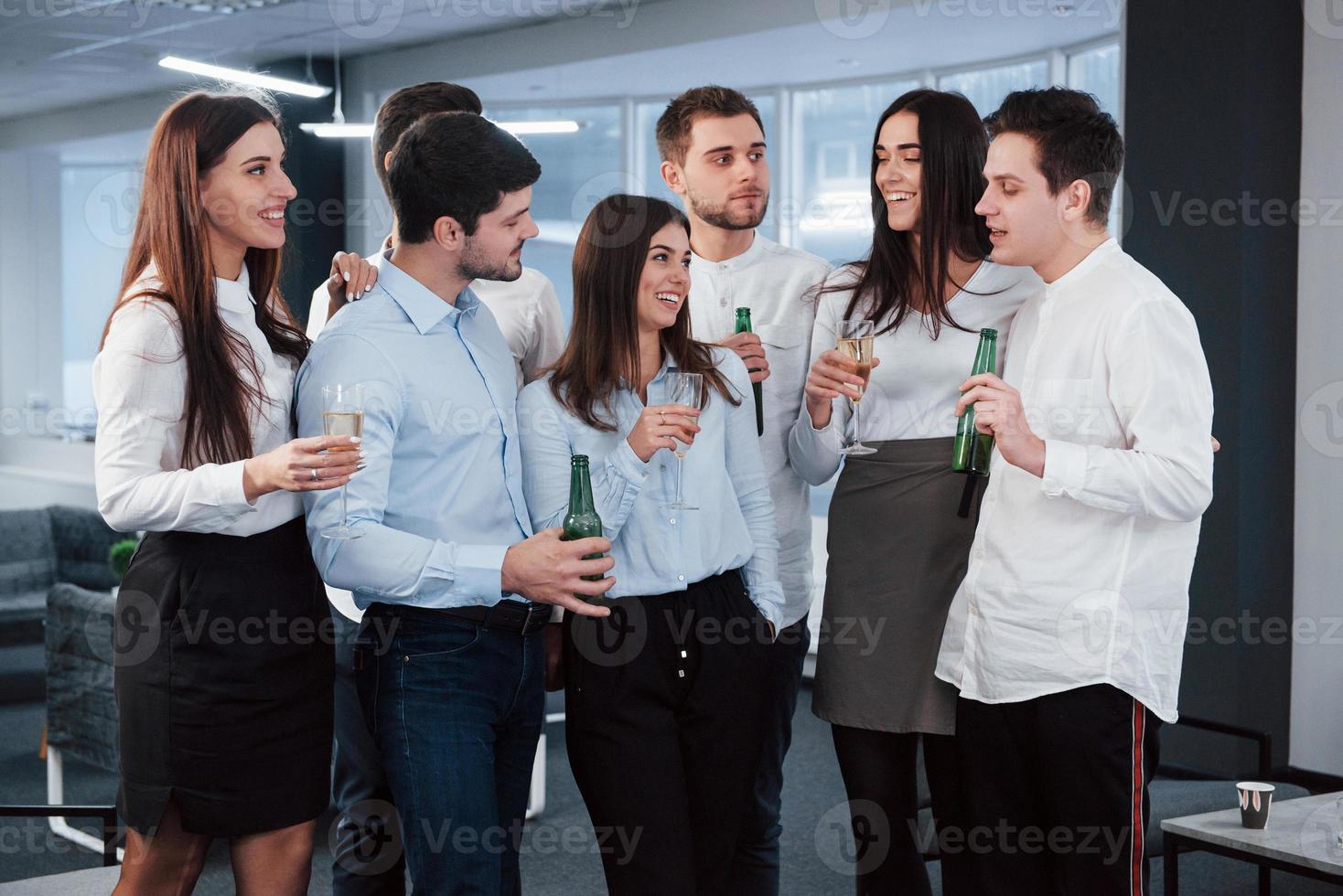 ragazzo ubriaco che dice qualcosa di interessante. tutti stanno ascoltando. foto di una giovane squadra in abiti classici che tiene in mano un drink nel moderno ufficio ben illuminato