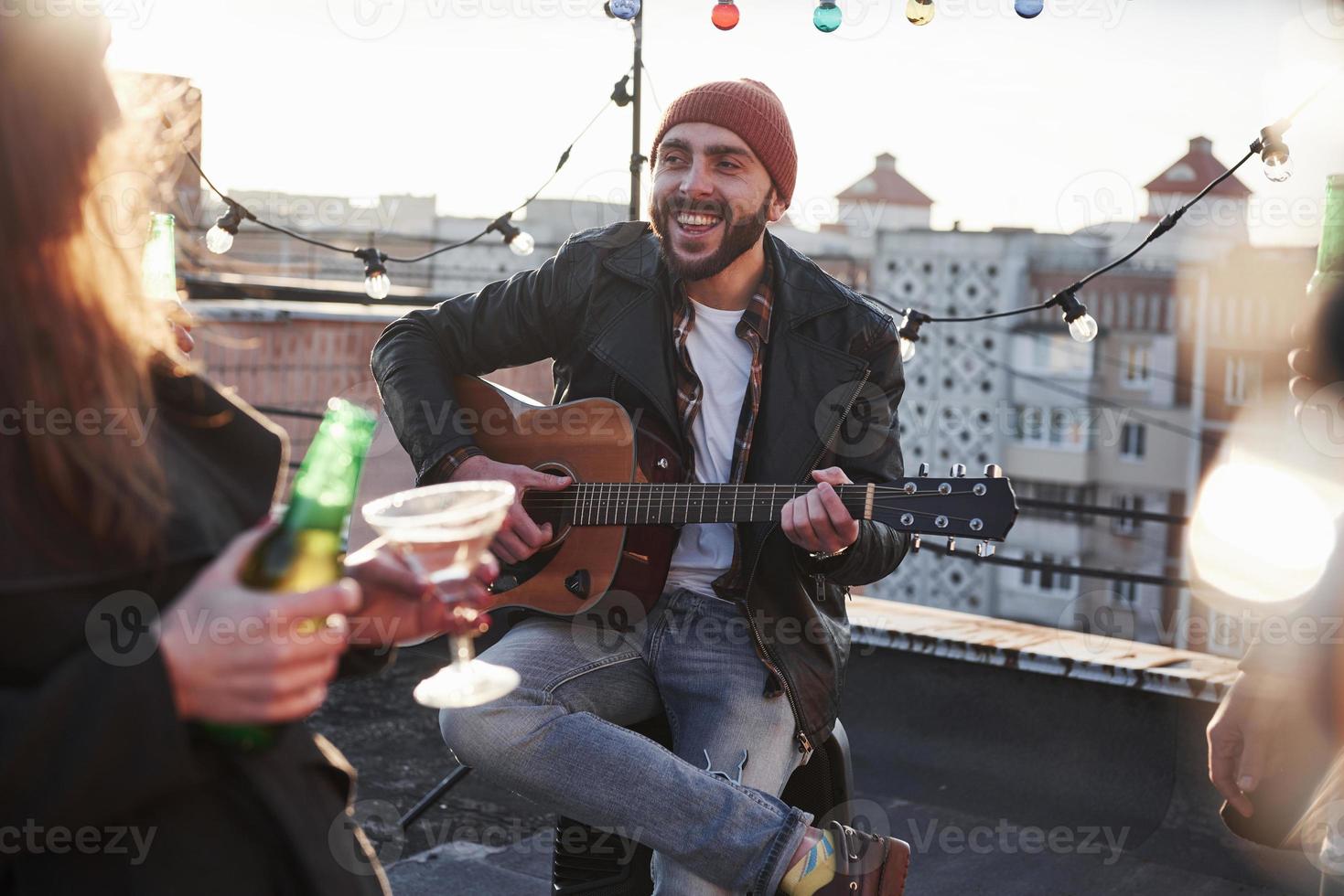 foto di un giovane chitarrista attraente con la barba che canta per i suoi amici sul tetto