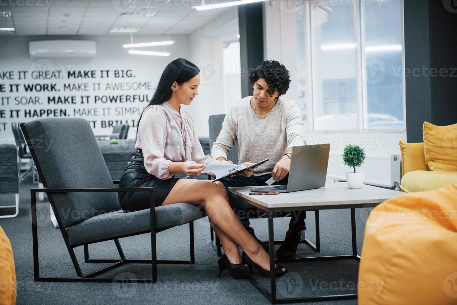 ragazzo riccio e ragazza bruna discutono i dettagli del contratto in un ufficio moderno foto