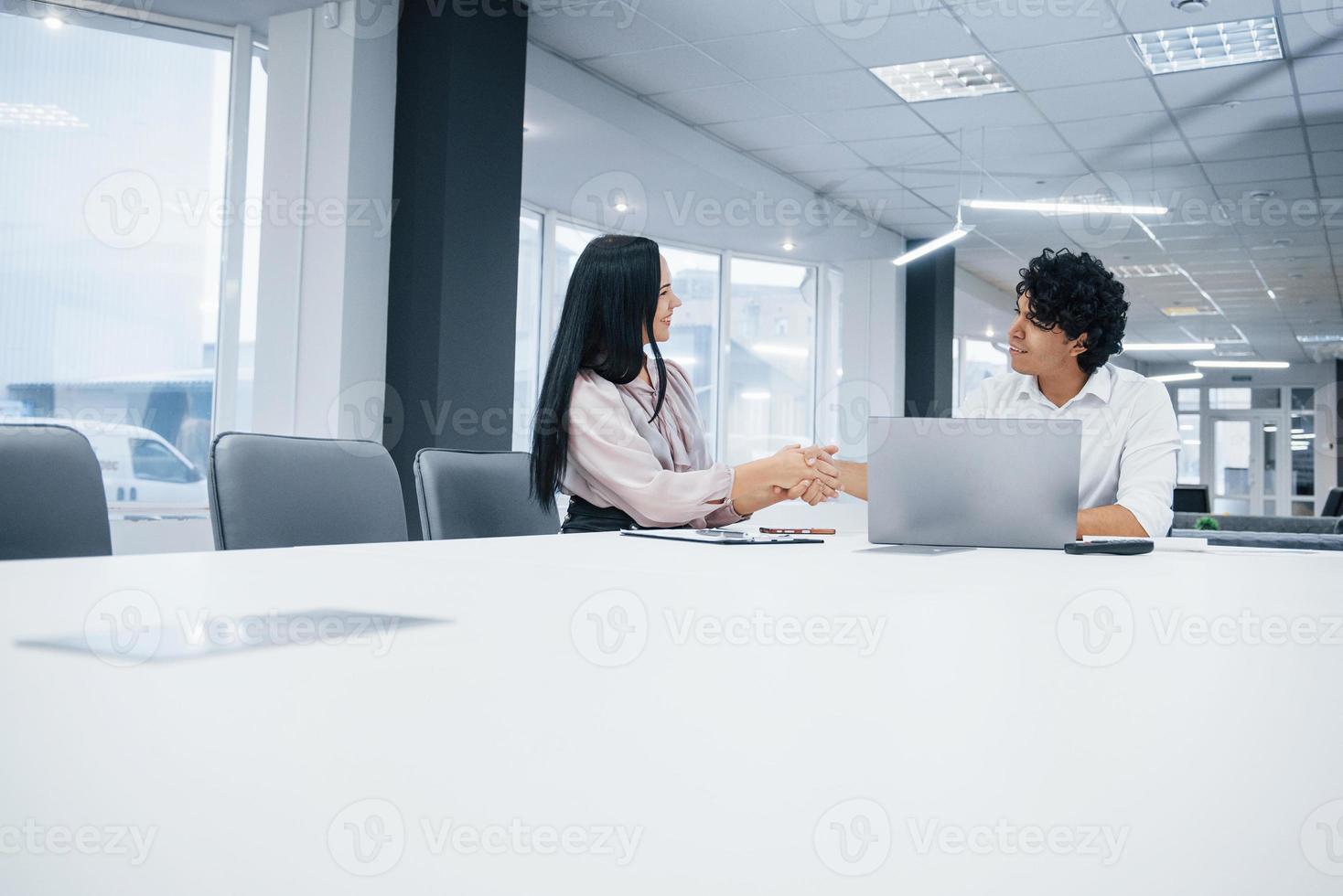 accordo di successo tra due persone sedute vicino al tavolo e al laptop nell'ufficio bianco foto