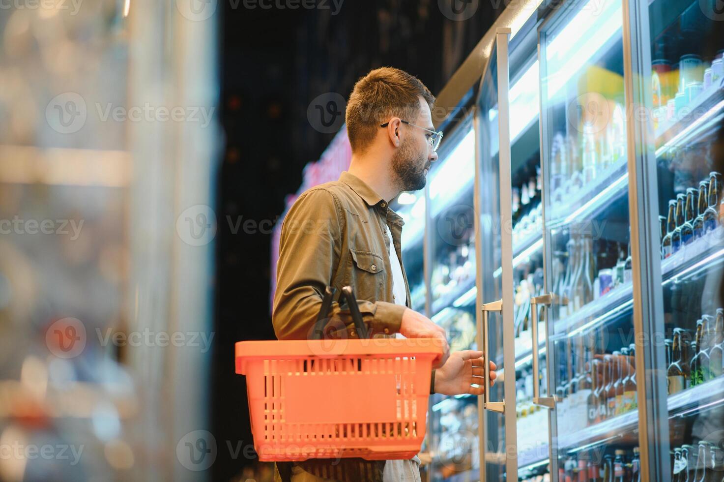 uomo con un' barba acquista un' birra nel il alcool Dipartimento di un' supermercato . bello uomo sceglie un' birra bottiglia nel il memorizzare e comunica su un' smartphone.shopping nel un' supermercato foto