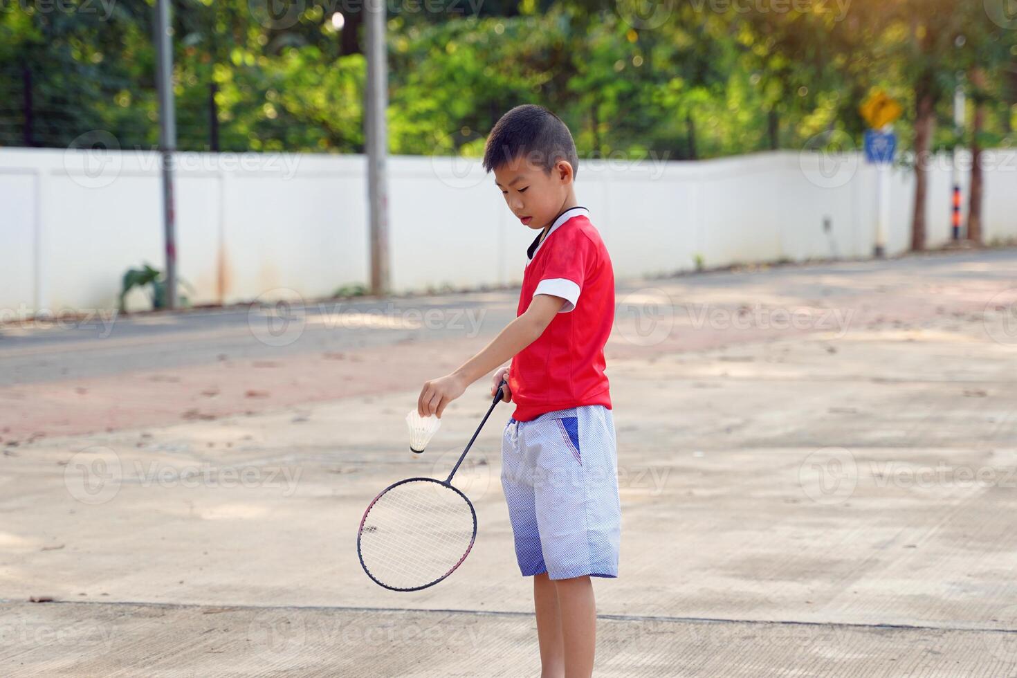 un asiatico ragazzo detiene un' badminton racchetta e un' bianca volano mentre giocando badminton con amici su il parco prato nel il sera dopo ritorno a partire dal scuola. foto