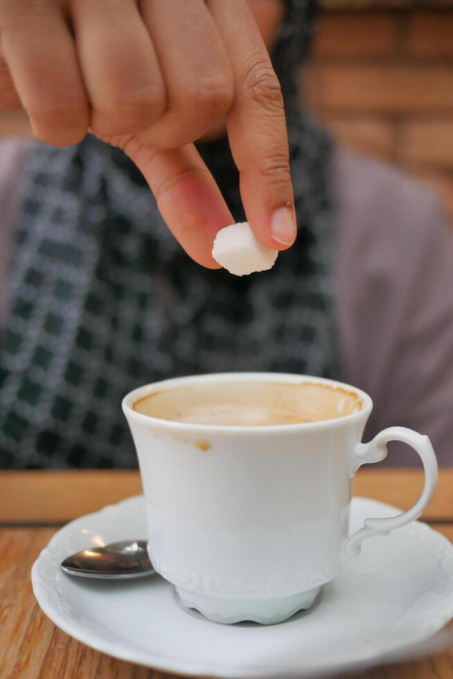 donna mano scrosciante bianca zucchero cubo nel un' caffè tazza , foto