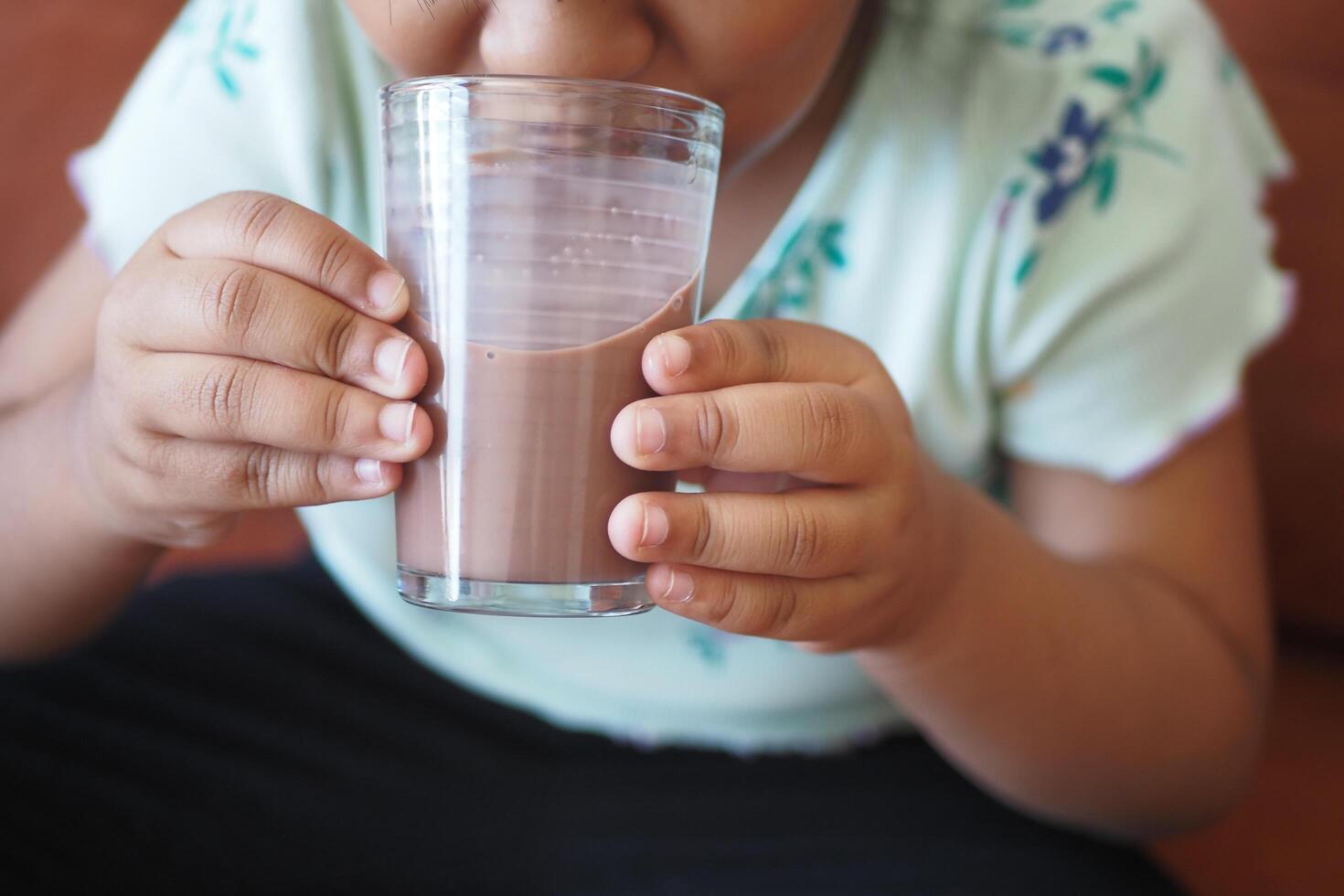 poco ragazza potabile gustoso cioccolato latte a casa. foto