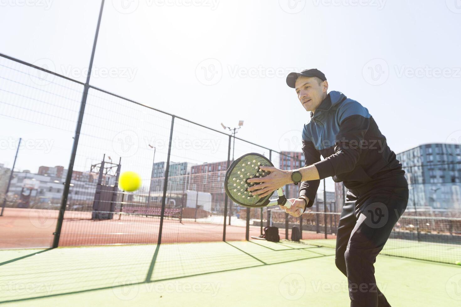 un' padel giocatore saltare per il sfera, bene guardare per messaggi e manifesto. uomo con nero racchetta giocando un' incontro nel il Aperto dietro a il netto Tribunale all'aperto. professionale sport concetto con spazio per testo foto