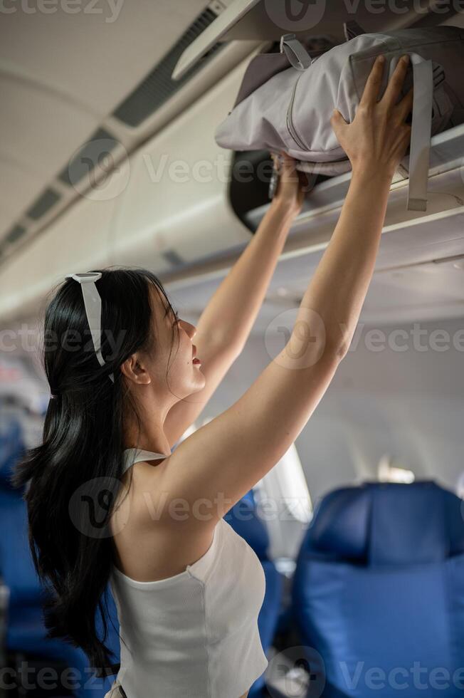 un attraente asiatico femmina passeggeri è mettendo sua Borsa nel un alto bidone, in viaggio di aereo. foto