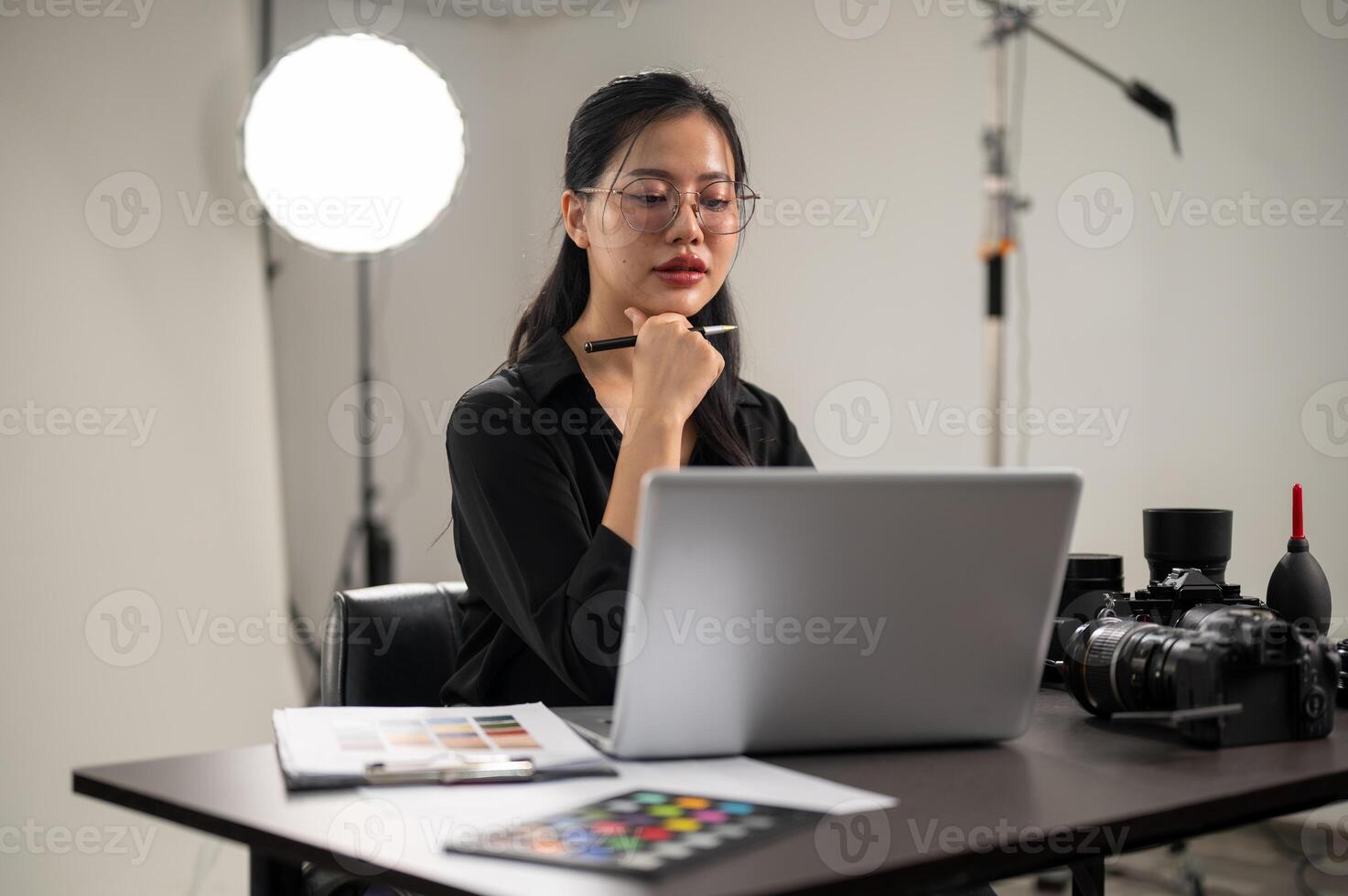 un' fiducioso asiatico femmina fotografo è Lavorando su sua computer portatile, Lavorando nel un' servizio fotografico studio. foto