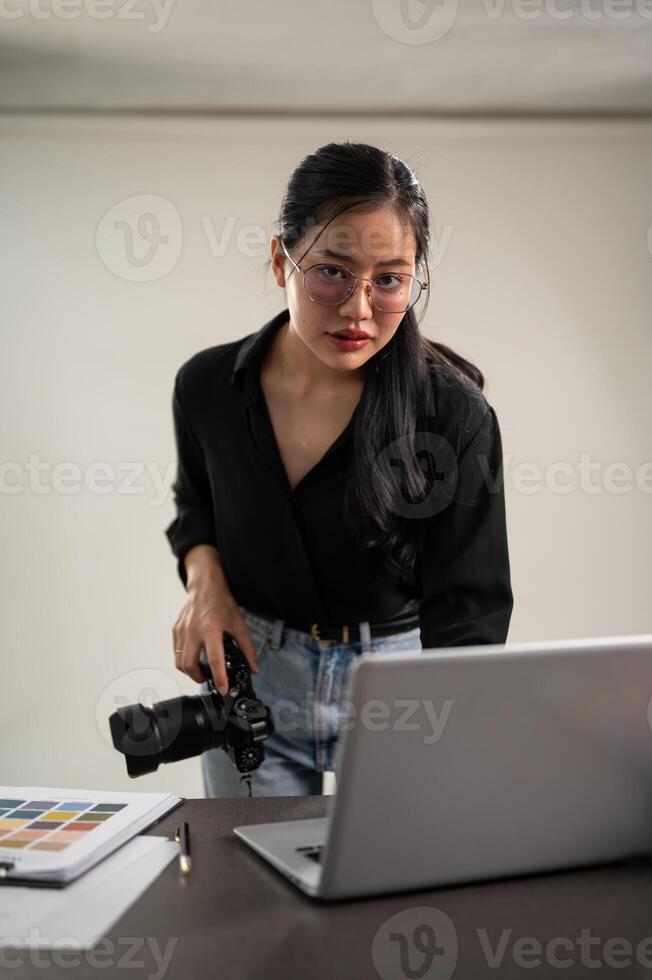 fiducioso asiatico femmina fotografo è controllo immagini su un' il computer portatile computer, Lavorando su un' servizio fotografico foto