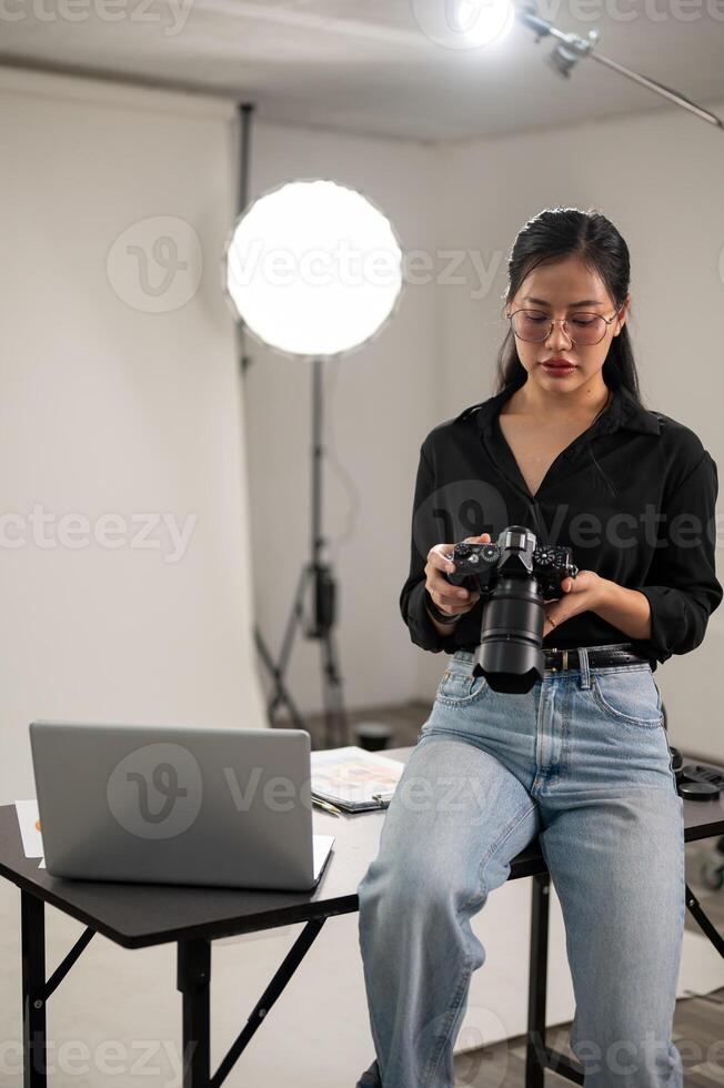 professionale asiatico femmina fotografo è messa a fuoco su regolazione sua dslr telecamera, Lavorando nel un' studio foto