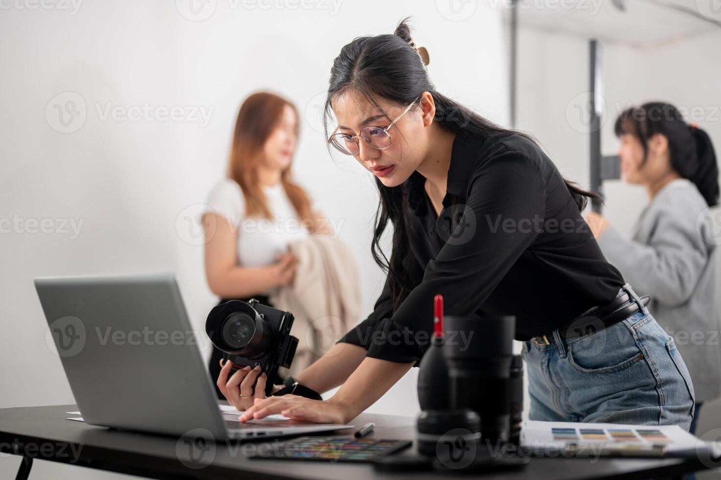 un' fiducioso femmina fotografo controllo immagini su sua computer portatile, Lavorando con sua squadra nel il studio. foto