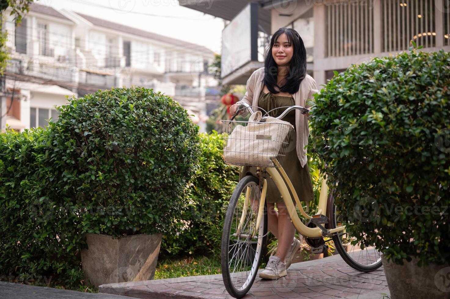 un' felice, bellissimo giovane asiatico donna è spingendo sua bicicletta su un' sentiero nel il città. foto