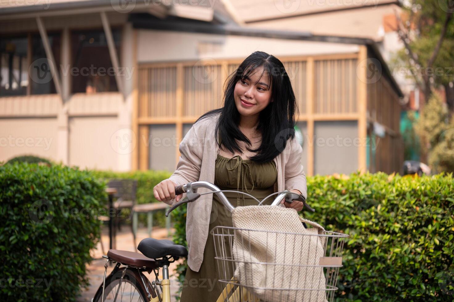 un' Bellissima, positivo asiatico donna nel un' carino vestito è a piedi e spingendo sua bicicletta nel il città. foto