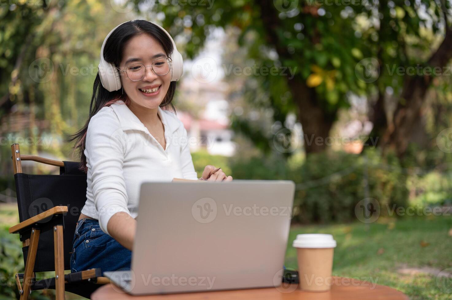 un' contento asiatico donna è Lavorando su sua compiti su sua il computer portatile mentre seduta nel sua Giardino dietro la casa. foto