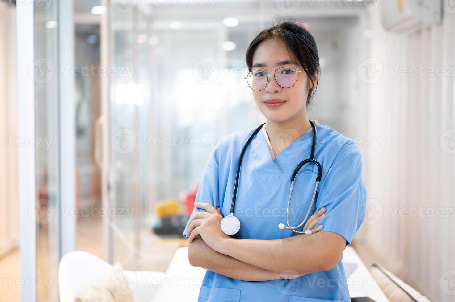 un' fiducioso asiatico femmina medico nel scrub in piedi nel il ospedale corridoio con sua braccia incrociato. foto