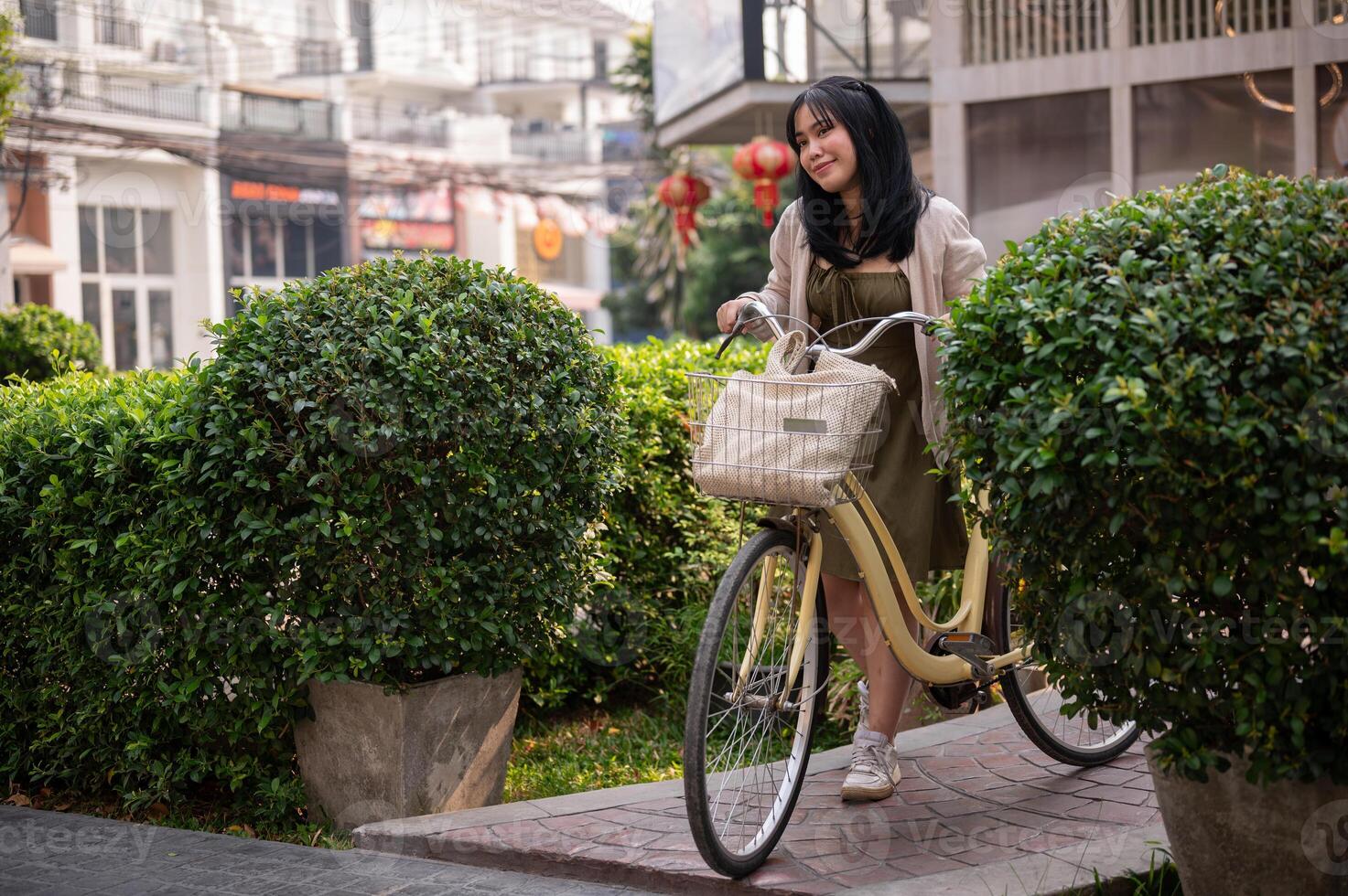 un' felice, bellissimo giovane asiatico donna è spingendo sua bicicletta su un' sentiero nel il città. foto