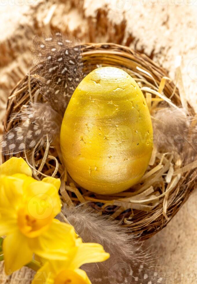 Pasqua carta. nido con decorativo d'oro uovo, cannuccia, piume, giallo narcisi su leggero vecchio Di legno. foto