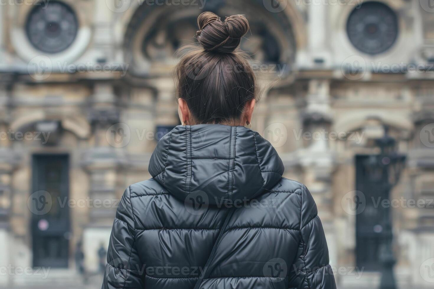 solo uno donna con un' ciambella nel un' nero inverno giacca contro il fondale di un' città edificio nel un antico stile. indietro Visualizza foto