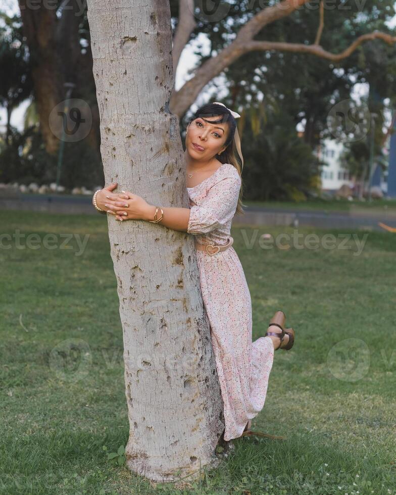 donna indossare vestito e capelli arco abbracciare un' albero nel un' pubblico parco. positivo emozione. foto