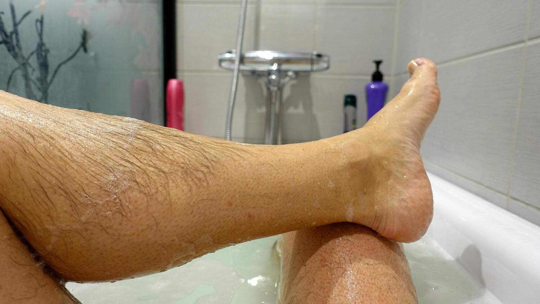 il gamba e piede In arrivo su di il acqua e sapone schiuma durante un' caldo bagno foto