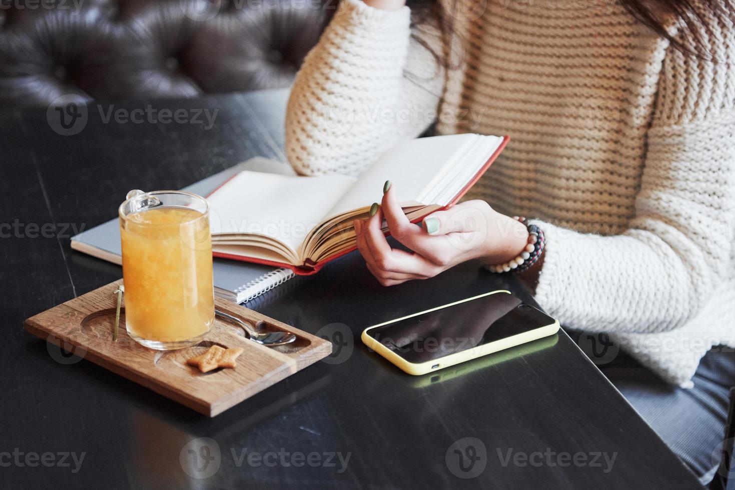 foto ravvicinata ritagliata di una donna che legge il libro al ristorante con bevanda gialla e smartphone sul tavolo