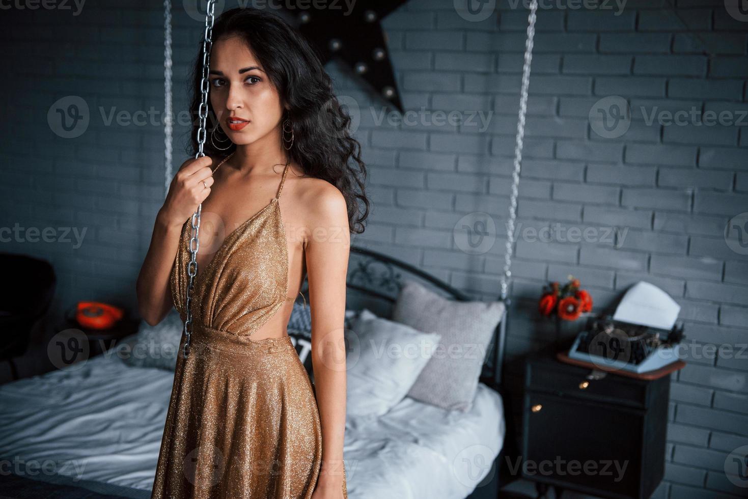 letto incatenato. ragazza in abito dorato sta di fronte al letto bianco in appartamenti di lusso foto