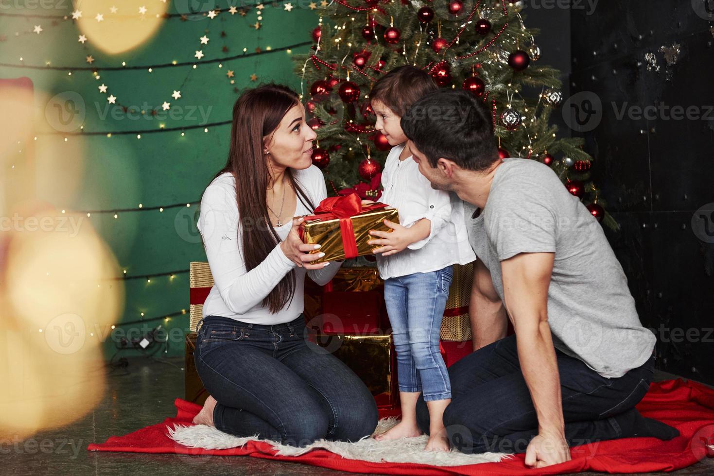 finalmente possiamo aprire questo regalo. la bella famiglia si siede vicino all'albero di Natale con scatole regalo la sera d'inverno, godendosi il tempo trascorso insieme foto