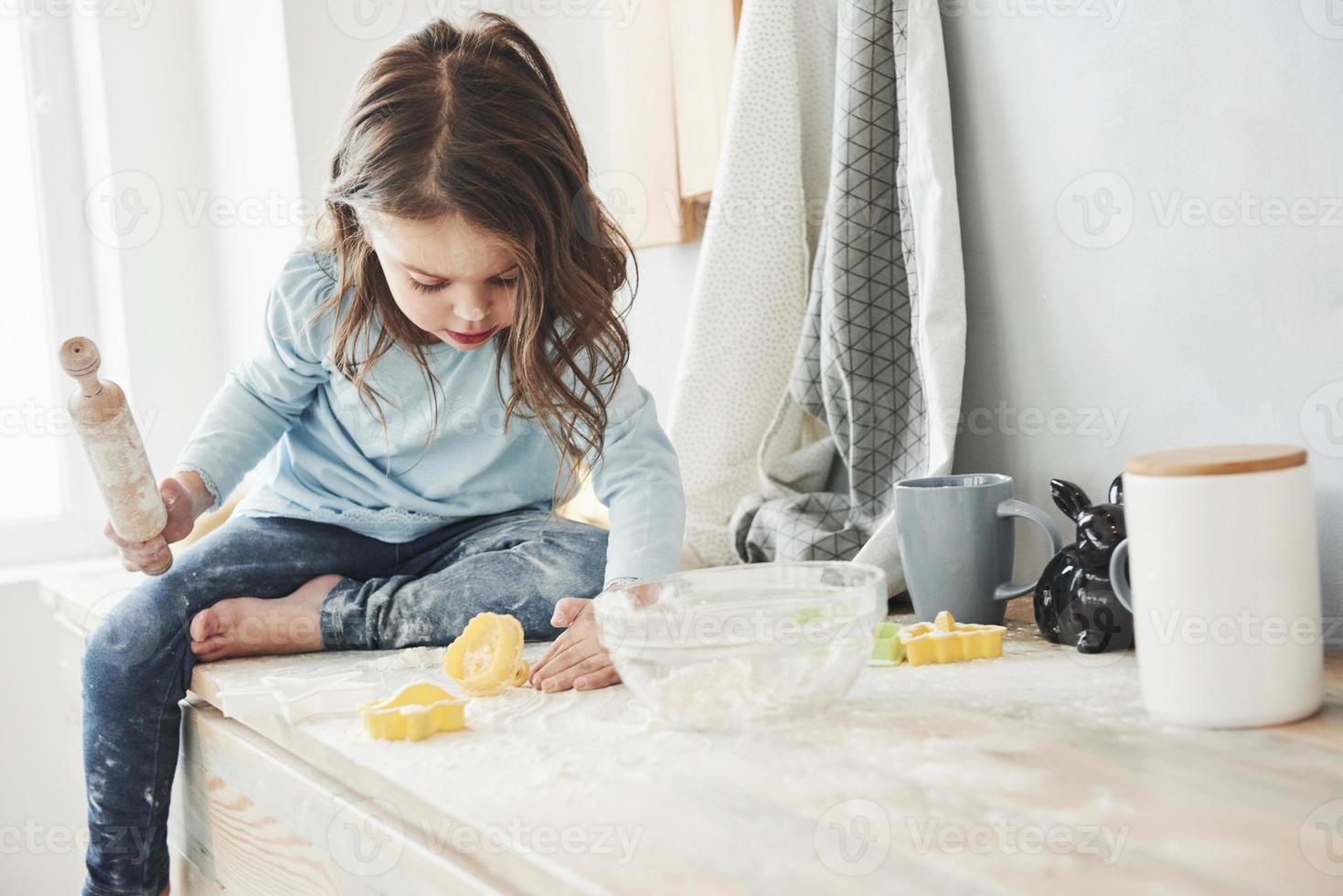 da solo nella stanza quando i genitori non sono a casa. foto di una bambina carina che si siede sul tavolo della cucina e gioca con la farina