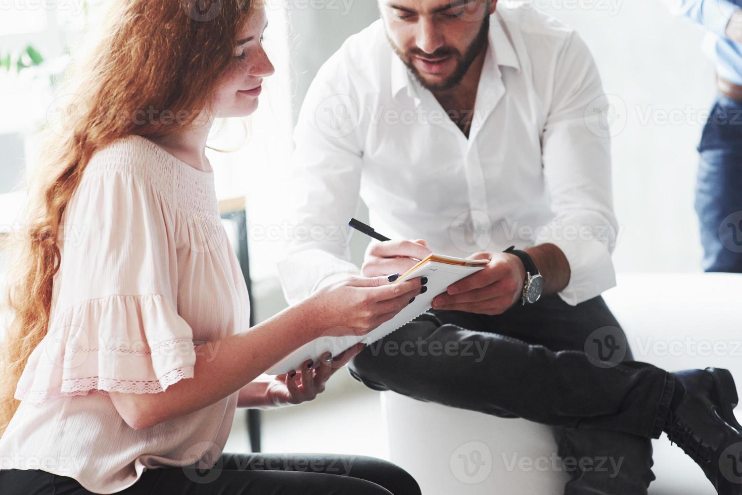 ragazza dai capelli rossi e uomo barbuto seduti sul divano e conversando sul loro progetto foto