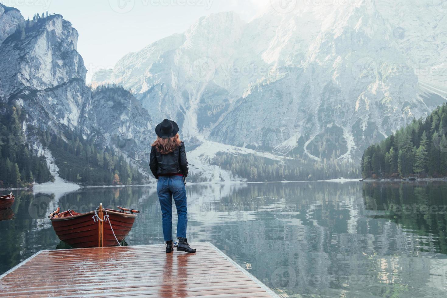boschi e lago di cristallo. donna con cappello nero che si gode un maestoso paesaggio di montagna vicino al lago con barche foto