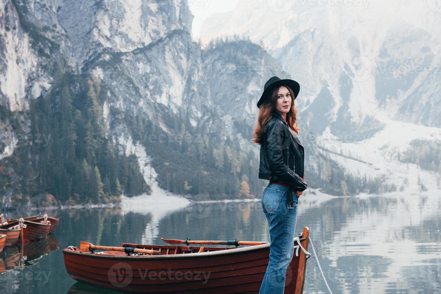 bellezza della natura e della ragazza in una foto. donna con cappello nero che si gode un maestoso paesaggio di montagna vicino al lago con barche foto