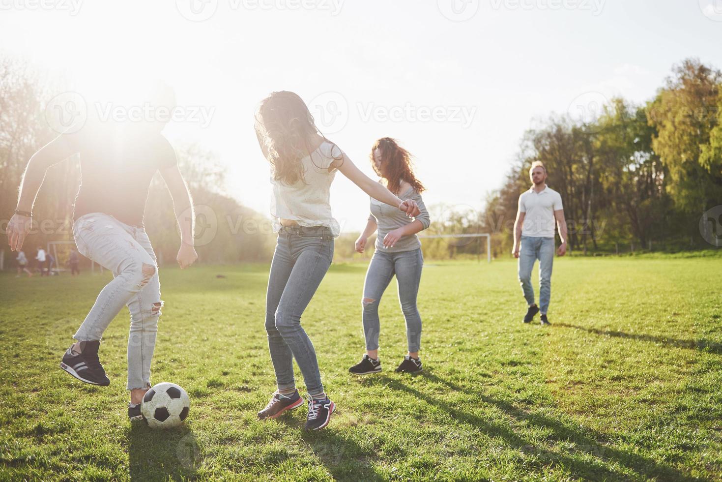 un gruppo di amici in abbigliamento casual gioca a calcio all'aria aperta. le persone si divertono e si divertono. riposo attivo e tramonto panoramico foto