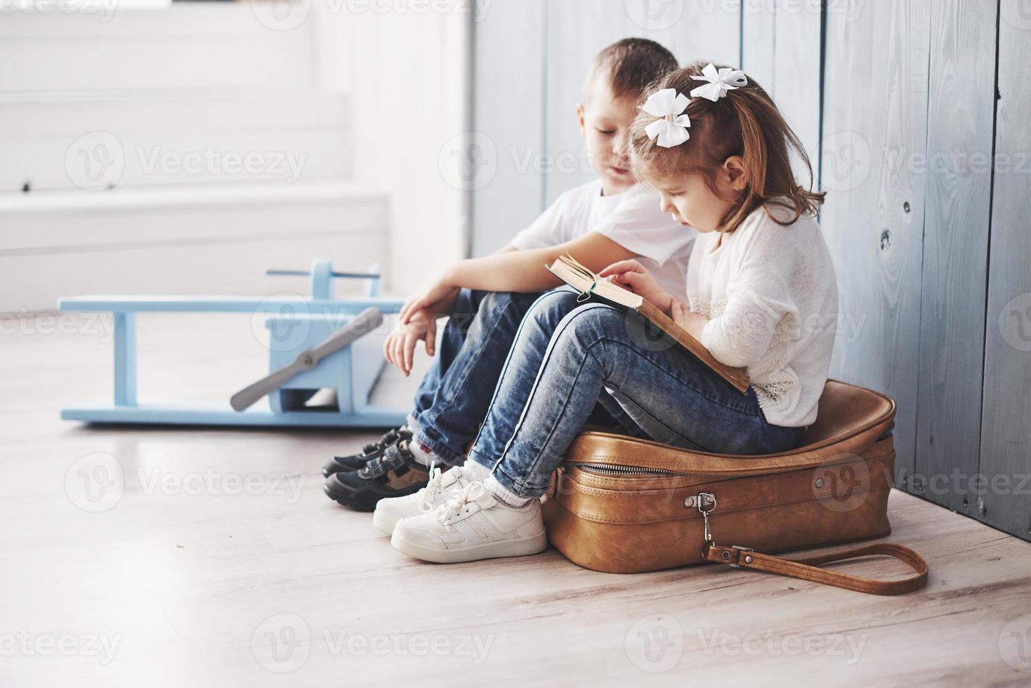 pronto per il grande viaggio. felice bambina e ragazzo che leggono un libro interessante che trasporta una grande valigetta. concetto di libertà e immaginazione foto